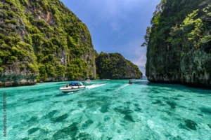 Speedboats glide across clear turquoise water between lush, steep limestone cliffs under a bright blue sky, creating a tropical paradise scene—perfect for unforgettable tailor-made Thailand holidays.