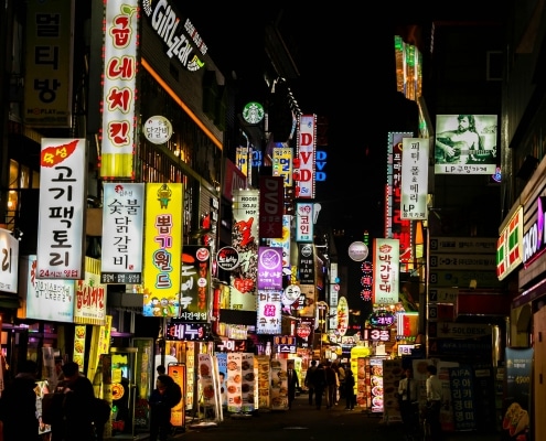 A bustling street at night in Korea, filled with colourful, illuminated signs in Korean advertising restaurants, bars, and shops, captures the lively spirit of holidays in South Korea as people stroll beneath the glowing lights.